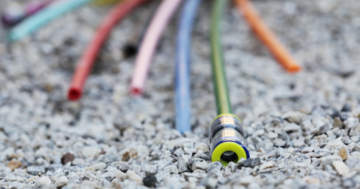 Auf dem Bild sieht man mehrere bunte Glasfaserkabel auf dem Boden liegen. Es deutet alles auf eine Baustelle hin.