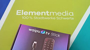 Ein Produktpaket mit einem Waipu.tv Stick liegt auf einem grünen Untergrund mit dem Schriftzug Elementmedia, 100 % Stadtwerke Schwerte
